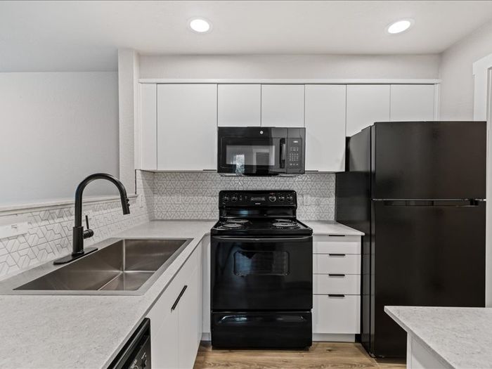 Modern kitchen featuring sleek black appliances, white cabinetry, and a stylish geometric backsplash.