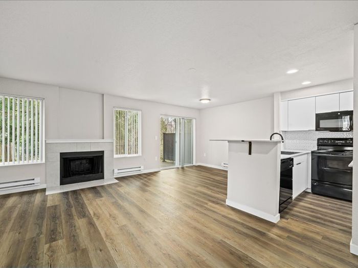 Bright open-concept living area with modern kitchen, cozy fireplace, and large sliding doors leading to a lush garden view.