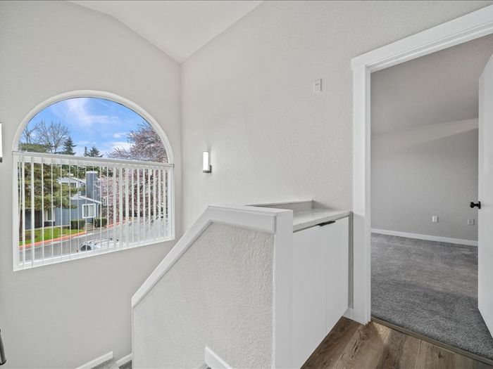 Bright and airy apartment hallway with elegant arched window, offering scenic outdoor view and access to carpeted room.