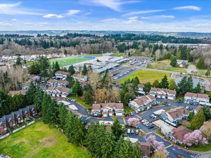 Aerial view of a charming suburban neighborhood with townhouses surrounded by lush greenery and open fields, offering serene living in a picturesque landscape.