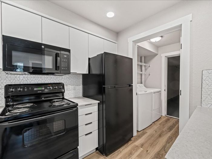 Modern kitchen with sleek black appliances and a hidden laundry nook, complemented by elegant white cabinetry and stylish backsplash.