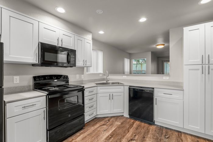 Modern kitchen with sleek white cabinets, stainless steel kitchen appliances, and elegant wooden flooring, offering a bright and inviting cooking space.