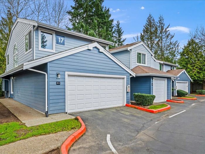 Charming townhouse units with cozy blue exteriors, private garages, and lush green surroundings.