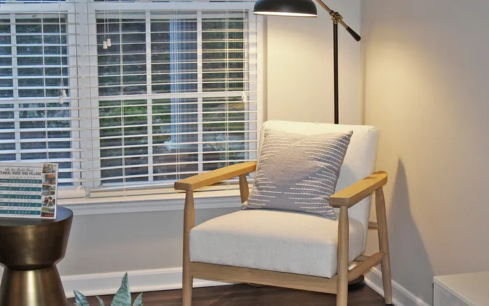 A cozy Centennial Ridge living room corner featuring a modern armchair, soft lighting, and large windows with blinds.