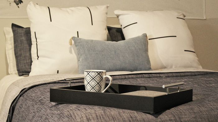 Inviting Centennial Village bedroom setting with patterned pillows and a tray featuring a decorative mug.