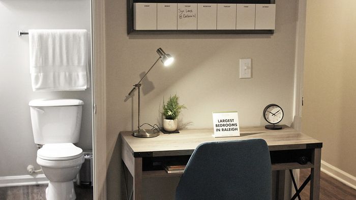 Compact Centennial Village bedroom home office with modern desk lamp and view of the bathroom featuring white towels and minimalistic décor.