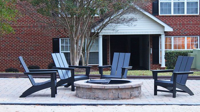 Centennial Village outdoor patio common area with four stylish wooden chairs surrounding a circular stone fire pit.