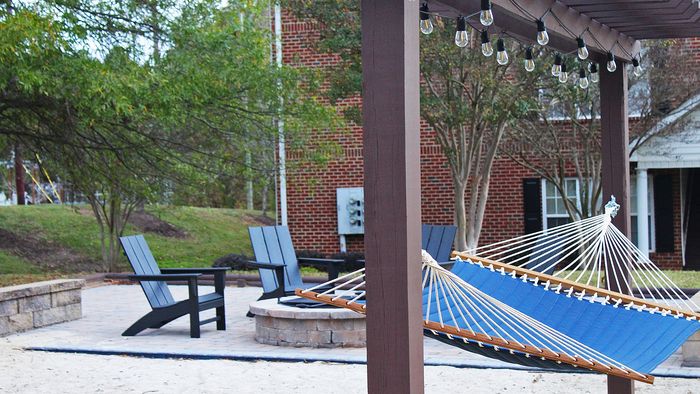 Centennial Village outdoor patio with a blue hammock, wooden pergola, and comfortable chairs, set against a backdrop of greenery and brick architecture.