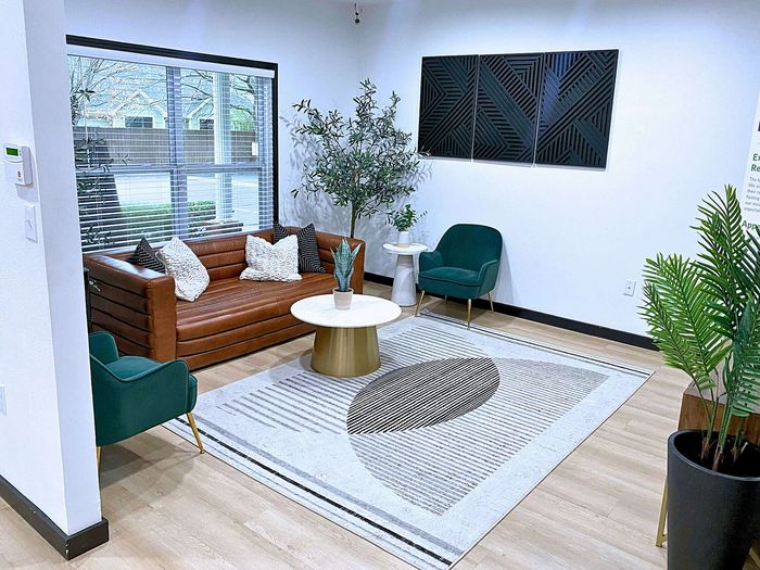 Centennial Village leasing office lounge with a stylish brown leather sofa, green armchair, and modern decor.