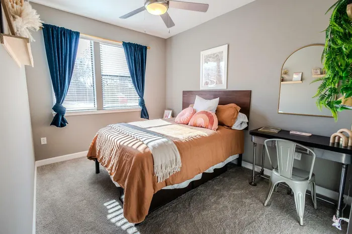 Inviting bedroom featuring a plush bed, stylish decor, and natural sunlight through a window with blue curtains.