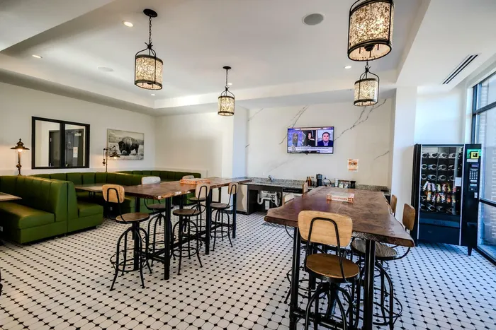 Modern communal space with green booths, wood tables, and stylish lighting, featuring a TV and snack vending machine.