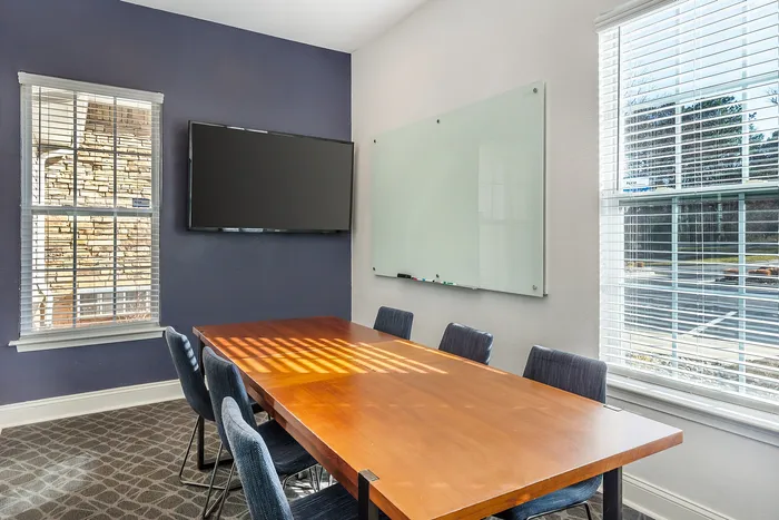 Bright conference room featuring a large wooden table, plush chairs, a whiteboard, and a flat-screen TV at Village Green in Raleigh, North Carolina.