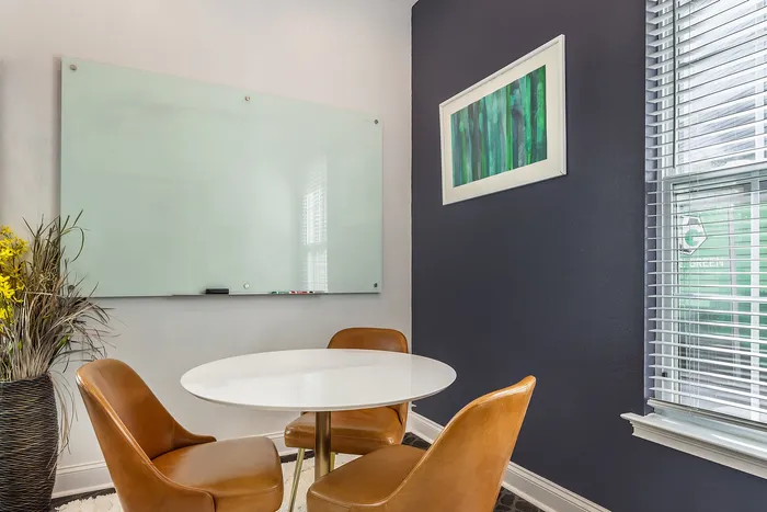 Stylish meeting space with a round table, leather chairs, and a large whiteboard against a dark wall at Village Green in Raleigh, North Carolina.