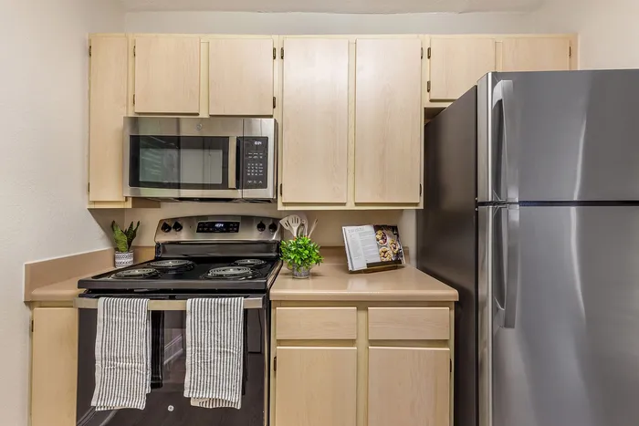 Stylish kitchen with modern appliances, light wood cabinetry, sleek countertops, and stainless steel refrigerator at Village Green in Raleigh, North Carolina.