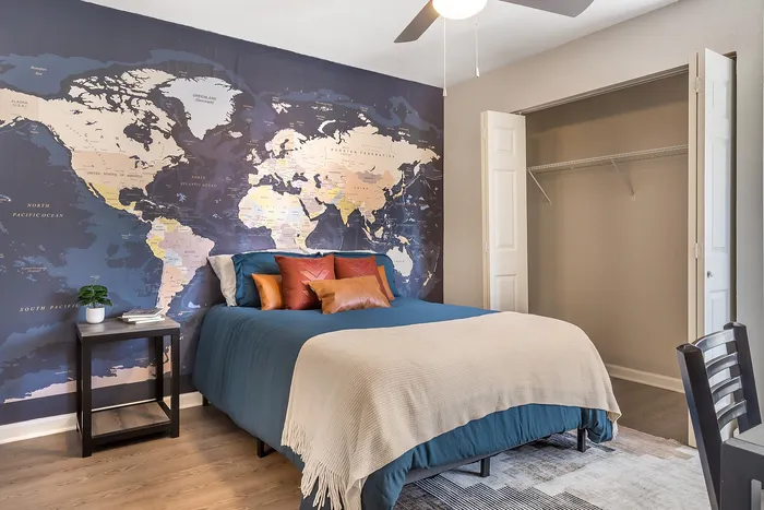 A stylish bedroom with a world map accent wall, cozy bed, and open closet at Village Green in Raleigh, North Carolina.
