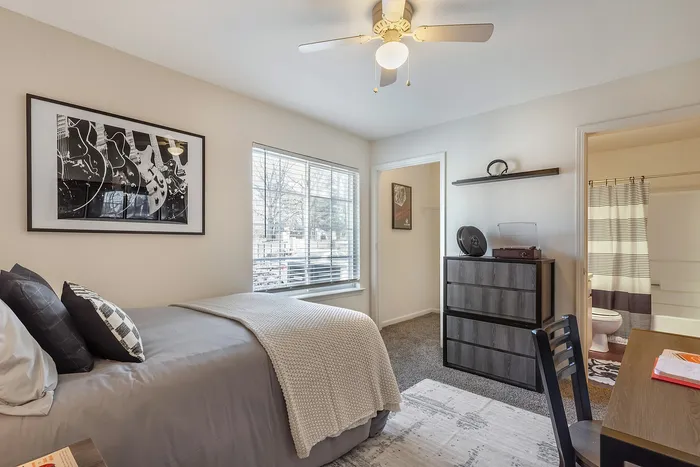 Inviting bedroom with stylish decor, featuring a comfortable bed, large window, and modern furniture at Village Green in Raleigh, North Carolina.