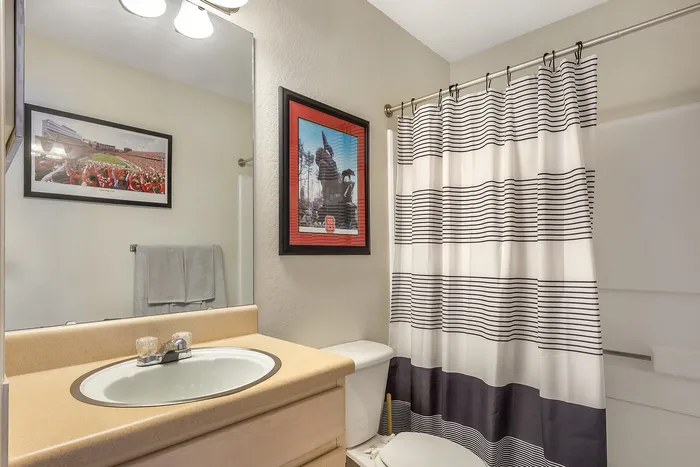 Chic bathroom featuring a modern vanity, framed artwork, and a stylish striped shower curtain at Village Green in Raleigh, North Carolina.