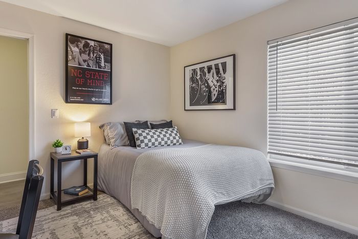 Inviting bedroom with a neatly made bed, elegant wall art, and natural light from window blinds at Village Green in Raleigh, North Carolina.