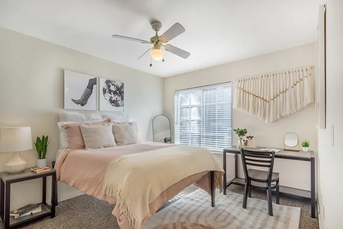 Inviting bedroom with a plush bed, modern decor, and a functional workspace beneath a bright window. at Village Green in Raleigh, North Carolina.