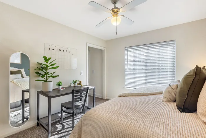Bright bedroom featuring a cozy bed, a sleek black desk, and vibrant green plants under natural lightat Village Green in Raleigh, North Carolina.
