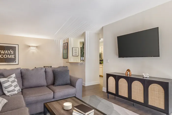 Stylish living room with a plush gray sofa, elegant wall art, and a flat-screen TV at Village Green in Raleigh, North Carolina.