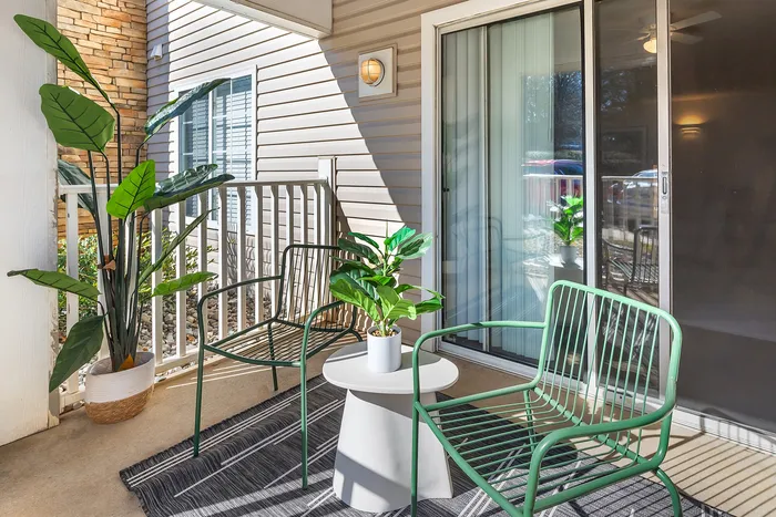 Inviting balcony with modern green chairs, a small table, and lush potted plants at Village Green in Raleigh, North Carolina.