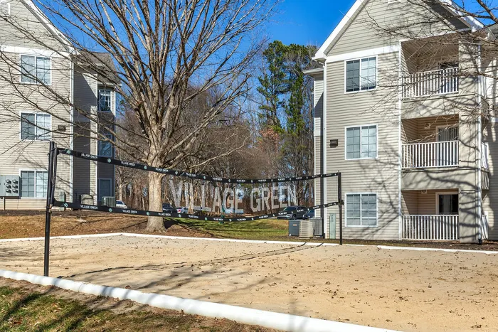 Outdoor view of Village Green apartments with sandy volleyball court and modern building.