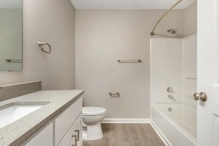 Bright and modern bathroom featuring sleek fixtures, granite countertop, and a white bathtub at Village Green in Raleigh, North Carolina.