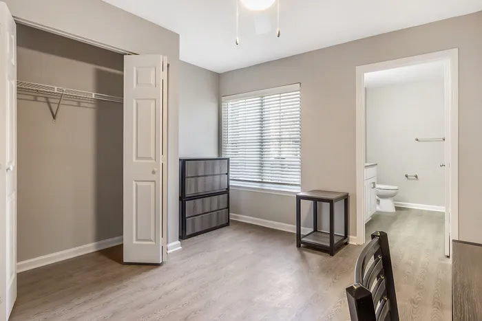 Bright bedroom with sleek wood flooring, modern dresser, and en-suite bathroom at Village Green in Raleigh, North Carolina.