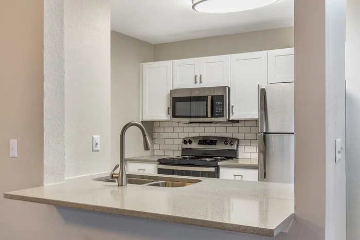 Stylish open kitchen with white cabinetry, stainless steel appliances, and a sleek countertop at Village Green in Raleigh, North Carolina.