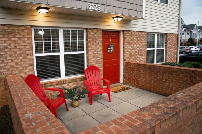 Inviting apartment entrance with a vivid red door, brick exterior, and cozy seating area.