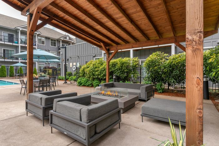 Chic outdoor lounge area with cozy seating around a stylish fire pit, featuring a modern pergola and a nearby poolside setting.