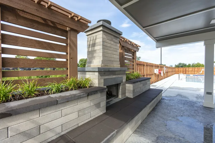 Chic outdoor patio area with a modern stone fireplace, elegant wooden trellis, and lush greenery by a sparkling swimming pool. West Lafayette, Indiana. Near Purdue.