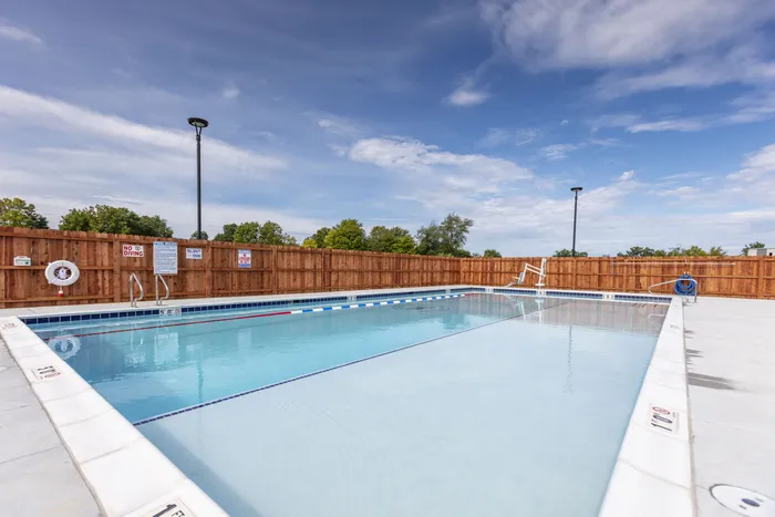 Inviting outdoor swimming pool with clear blue water, surrounded by a wooden fence and lush greenery under a bright sky. West Lafayette, Indiana. Near Purdue.