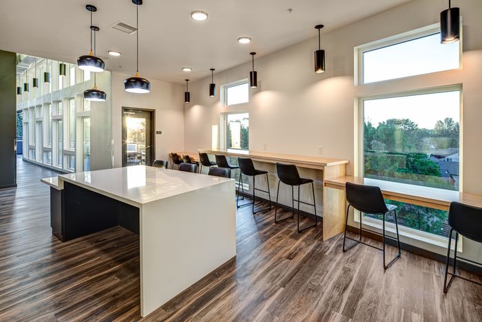 Modern apartment interior with sleek kitchen island, stylish pendant lighting, and panoramic windows revealing lush greenery.