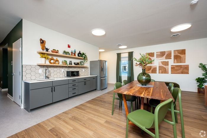 Modern kitchen and dining area with sleek grey cabinets, stylish shelving, and a wooden table set against a chic interior design.
