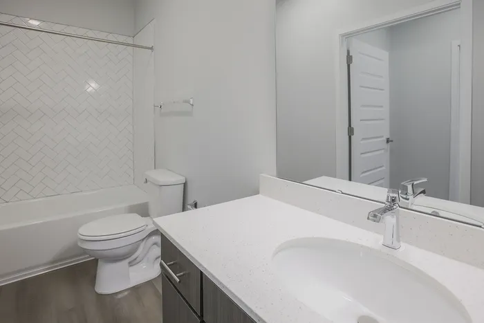 Modern bathroom featuring sleek vanity, pristine white countertop, and elegant herringbone tile backsplash.