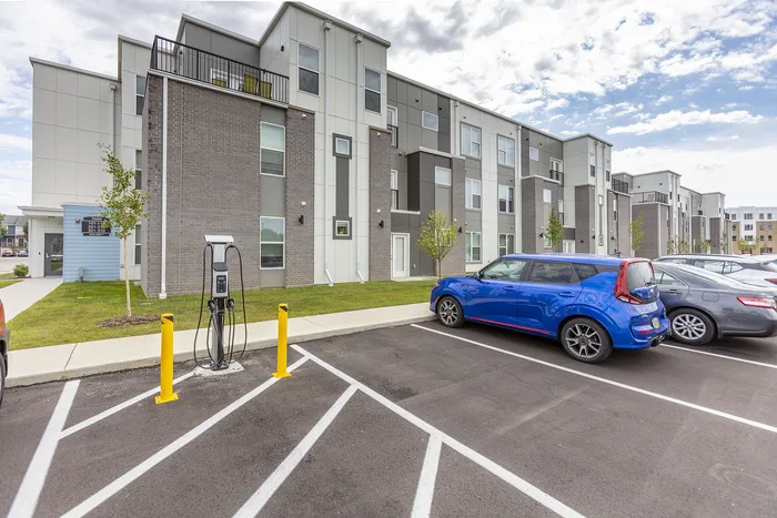 Modern apartment complex with sleek architecture featuring eco-friendly electric car charging station in a well-maintained parking lot.
