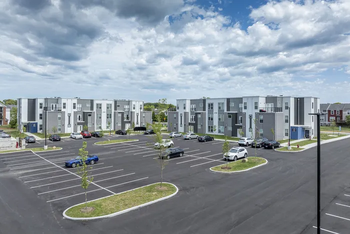 Modern apartment complex with stylish architecture, spacious parking, and a scenic sky backdrop, highlighting comfortable urban living.