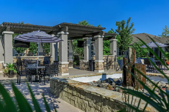 Shaded poolside lounge area with stone pillars and water feature at Corbin Crossing Overland Park KS