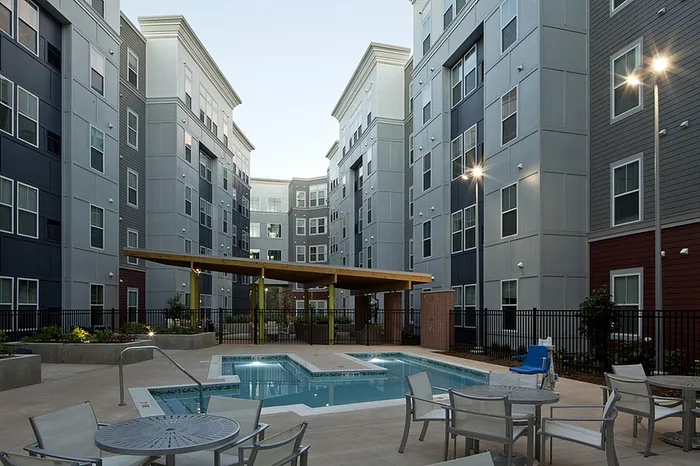 Modern apartment complex with a stylish outdoor patio featuring a sparkling pool and comfortable seating, perfect for relaxation and gatherings.