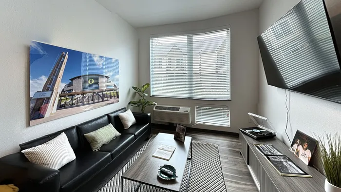 Modern living room with black sofa and mounted TV at The Flats at Chase student apartments in Eugene, OR