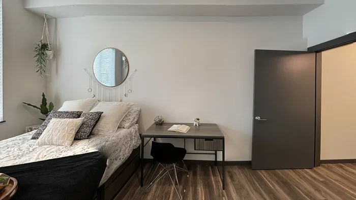 Modern bedroom with cozy bed, work desk, and hanging plant at The Flats at Chase in Eugene, OR