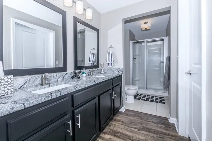 Apartment bathroom with dual-sink granite vanity and glass shower enclosure at Corbin Crossing Overland Park KS