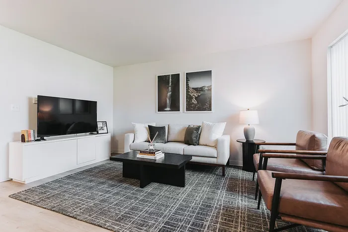 Forest Hills living room with a sleek TV, cozy white sofa, and stylish armchairs, beautifully accented by a contemporary coffee table and soft lighting.