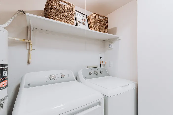 Forest Hills apartment laundry room with sleek white washing machine and dryer, accented by stylish woven baskets on an overhead shelf.