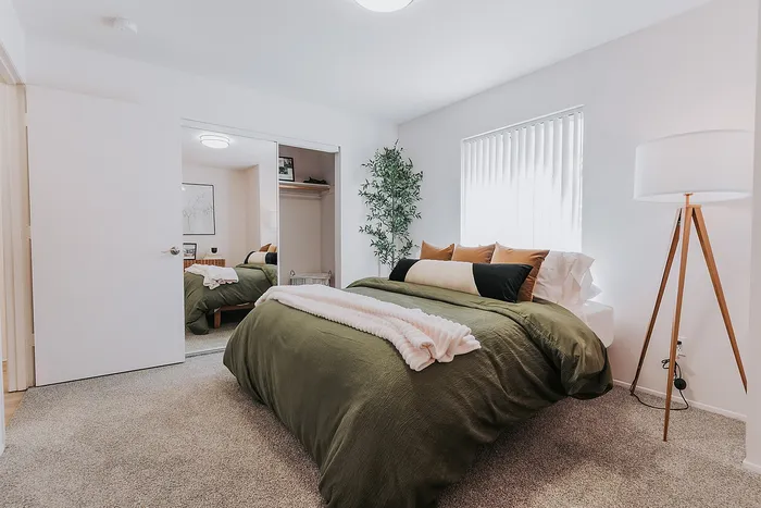 Forest Hills bedroom with a plush bed, cozy green bedding, modern decor, and a floor lamp, exuding a tranquil atmosphere.