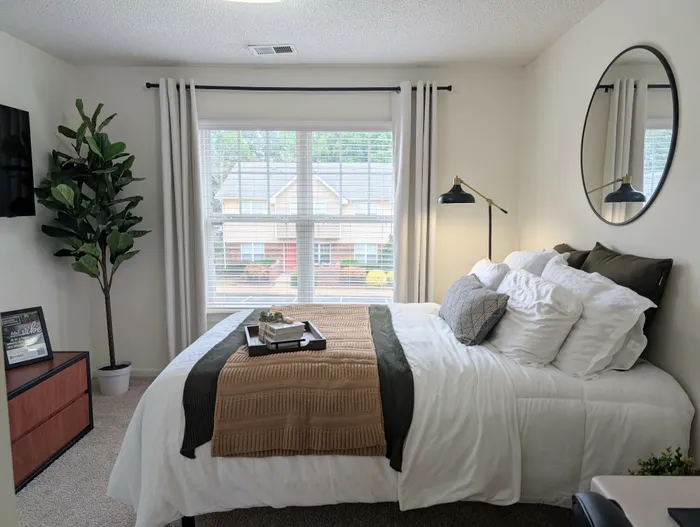 Bright and airy bedroom with modern decor and large window at University Suites apartments in Raleigh NC