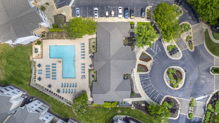 Aerial view of Village Green student apartments featuring a large T-shaped resort pool, poolside seating, landscaped grounds, and ample parking near NCSU in Raleigh NC