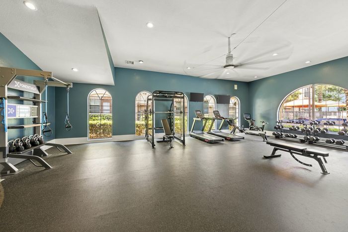 Highlander at North Campus 24/7 fitness center with treadmills, stationary bike, weights, and TRX system with arched windows in Riverside CA